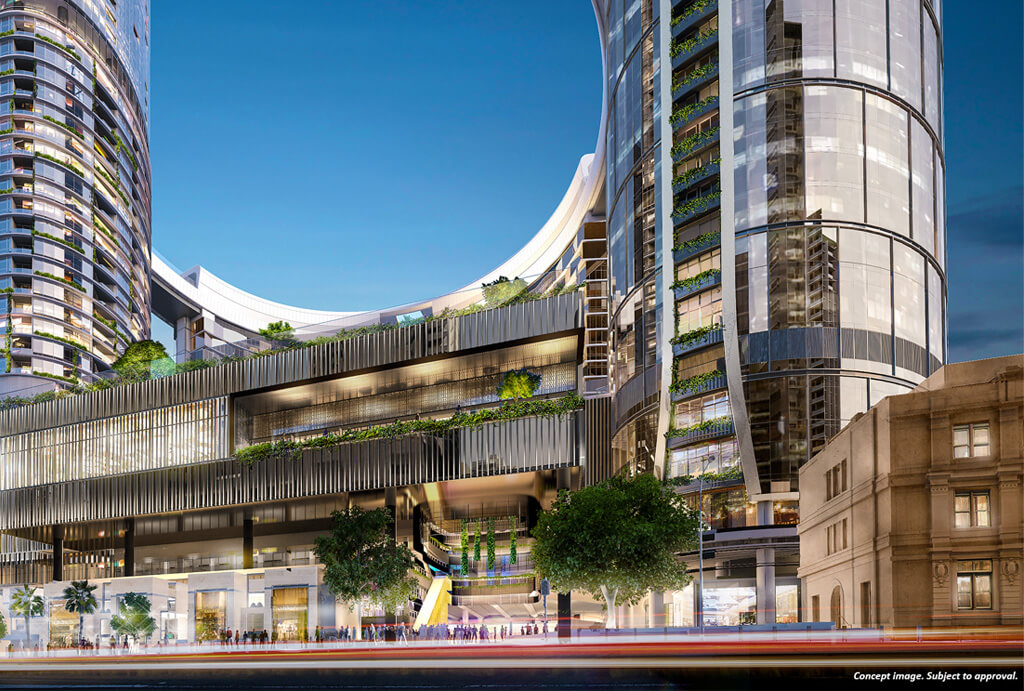 A modern cityscape with tall, curved glass buildings, green terraces, and lush plants integrated into the architecture. Street-level view features trees, blurred traffic, and pedestrians near the contemporary structures.