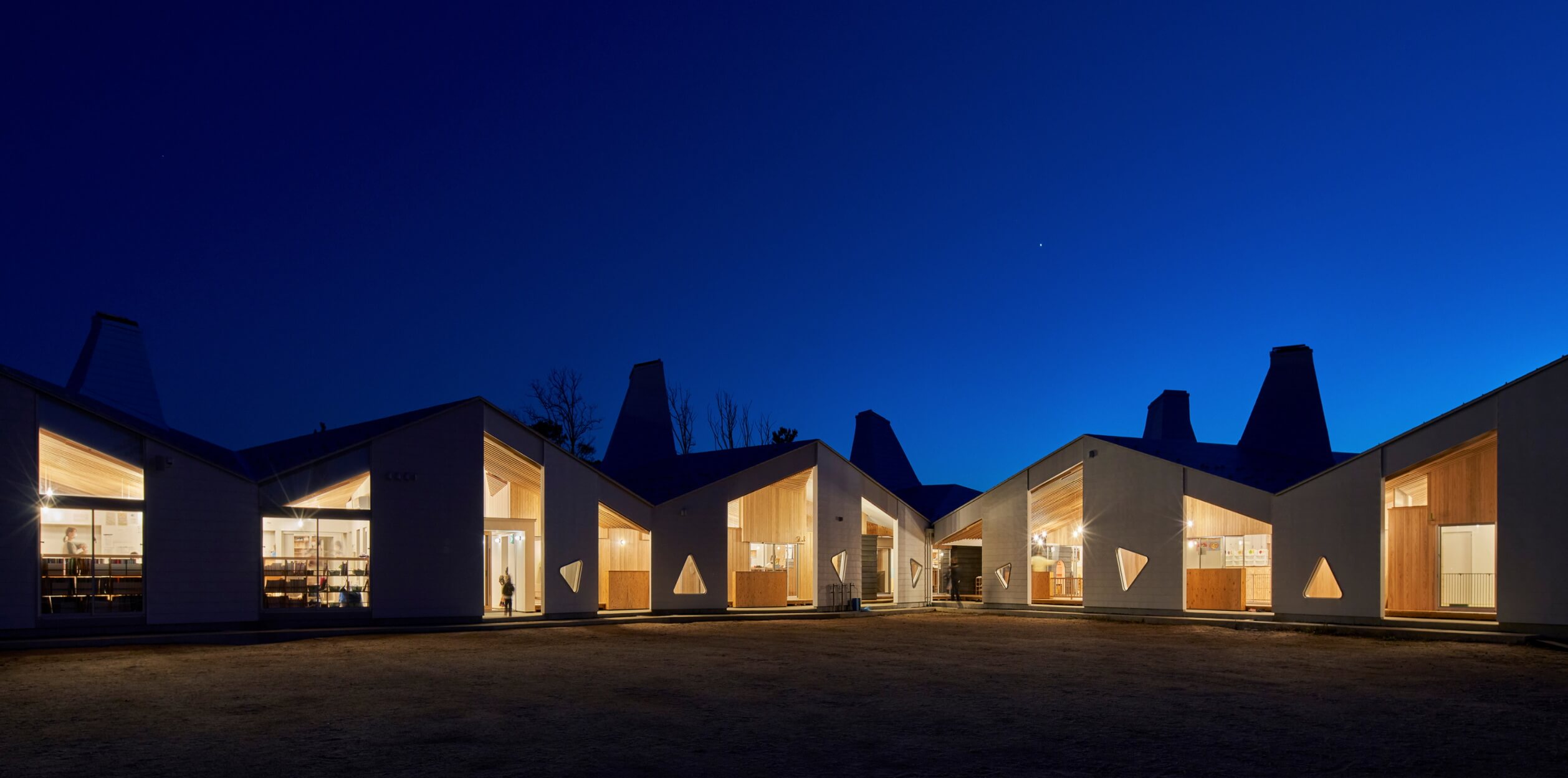 Night view of a modern architectural building with multiple gabled roofs. Illuminated from within, the structure highlights large windows and triangular design elements against a deep blue sky. An architects dream, envisioned through BIMx technology, brings every detail to life.