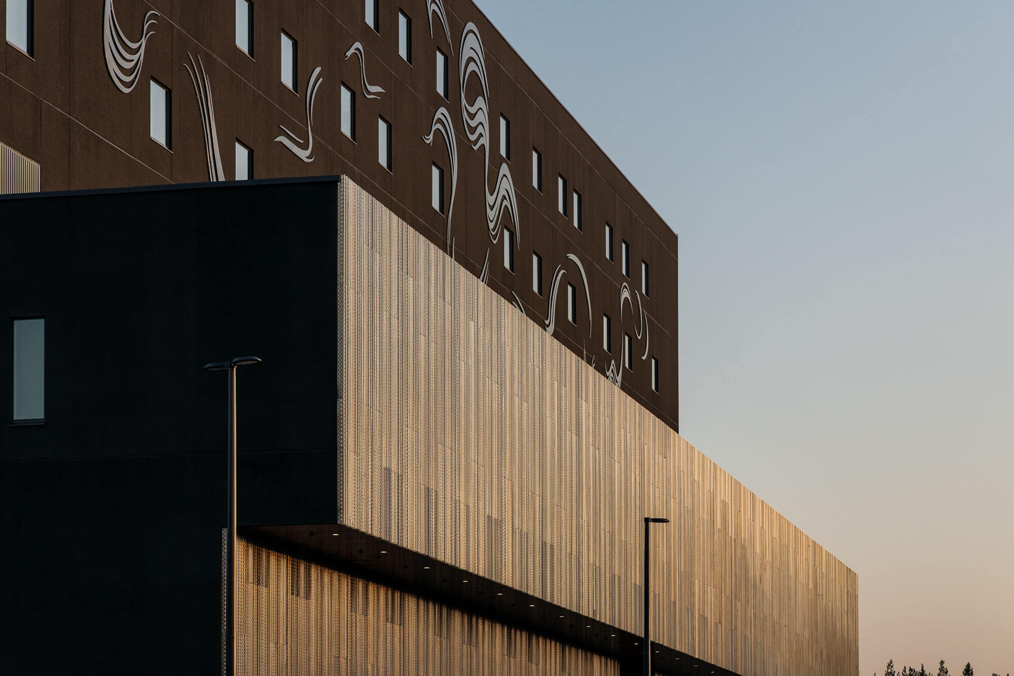 Modern building with a minimalist design, enhanced using Archicad for precision, featuring large, smooth surfaces and rectangular windows. Abstract white line art decorates the upper section. The clear sky hints at either sunrise or sunset.