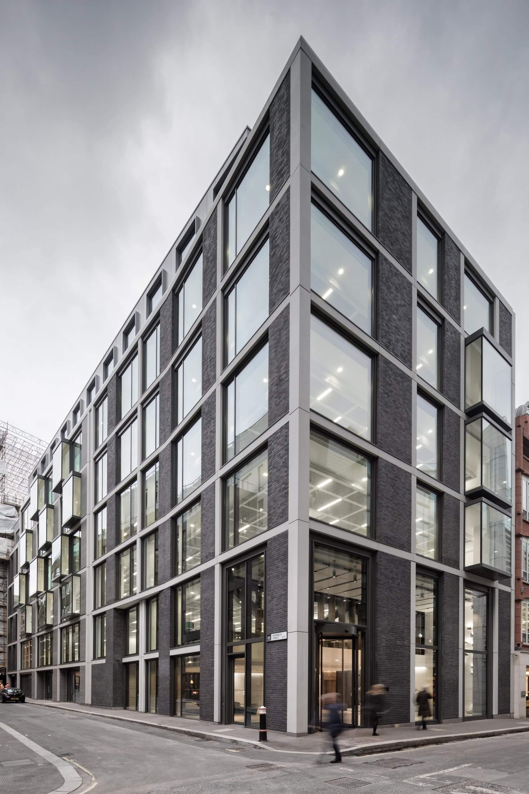 This modern multi-story building, enhanced by Archicad, showcases a grid-like facade with large glass windows and dark structural elements. The corner view underscores its contemporary design, while people stroll along the street in front of this Graphisoft-inspired architectural marvel.