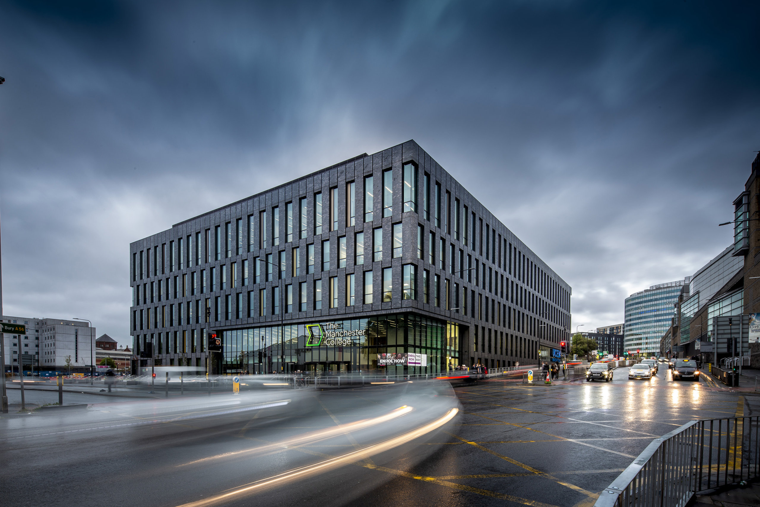 A modern, multi-story office building with expansive windows rises against a dramatic, overcast sky. As cars and buses blur by on the wet street, reflecting the lights, you can almost imagine this scene perfectly rendered in Archicads digital realm.