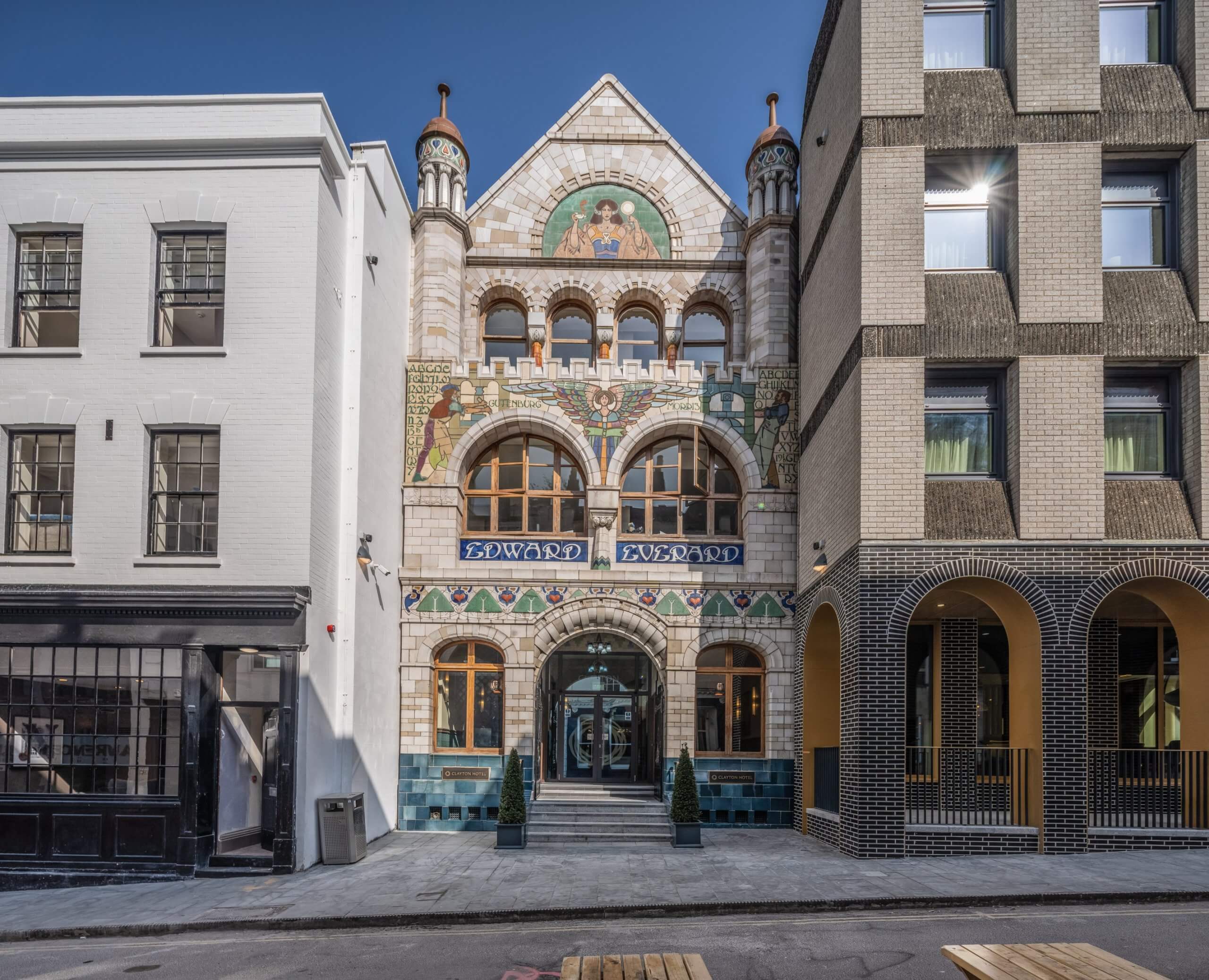 Street view of an ornate, historic building with a colorful facade labeled “Edward VII,” featuring arched windows and decorative towers. Its flanked by a sleek modern structure possibly designed using CAD software like Archicad and a classic white building.