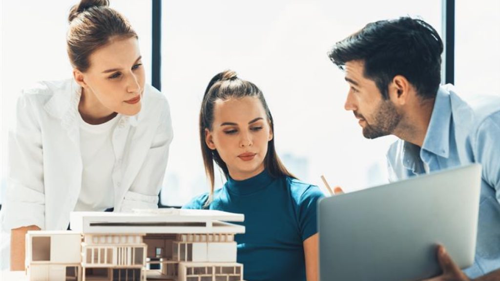 Three students are engaged in a discussion around a table with architectural models and a laptop, representing one of the key aspects of the Nemetschek Global Academic Program: the seamless transition from students to architectural professionals.