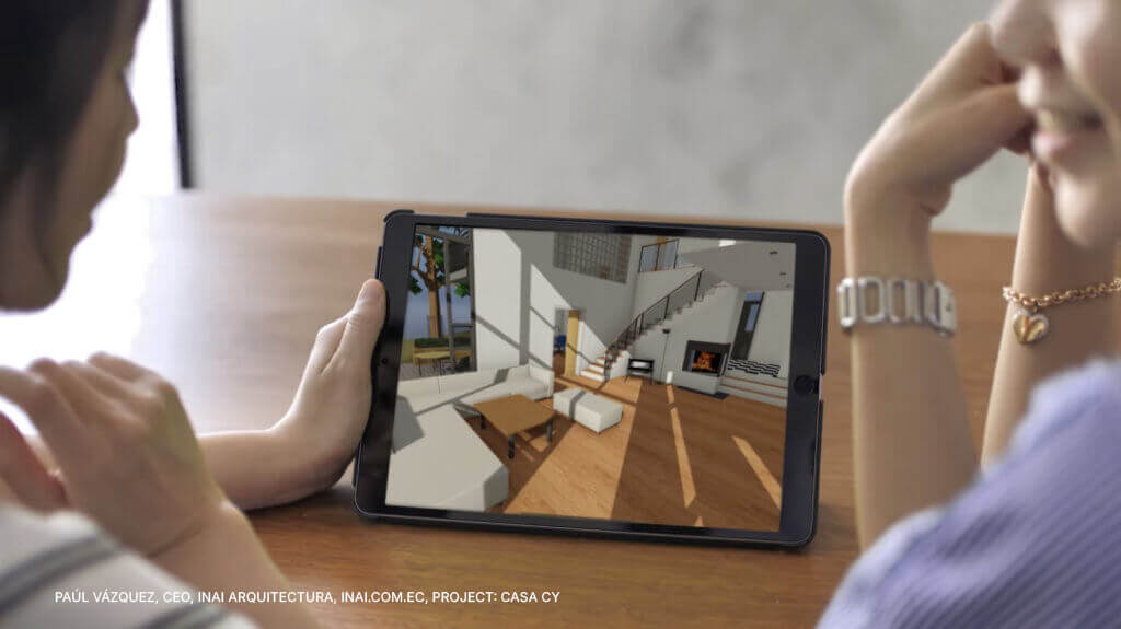 Zwei Personen sitzen an einem Tisch und betrachten ein Tablet, auf dem eine 3D-Architekturdarstellung eines modernen Wohnzimmers mit einer Treppe und grossen Fenstern zu sehen ist.